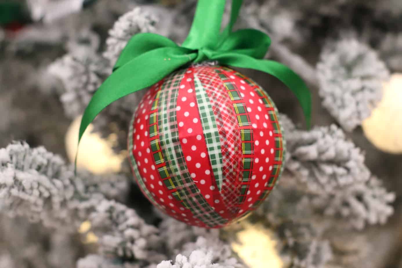 on ornament wrapped with red and green washi tape hung with a green ribbon from a flocked Christmas tree