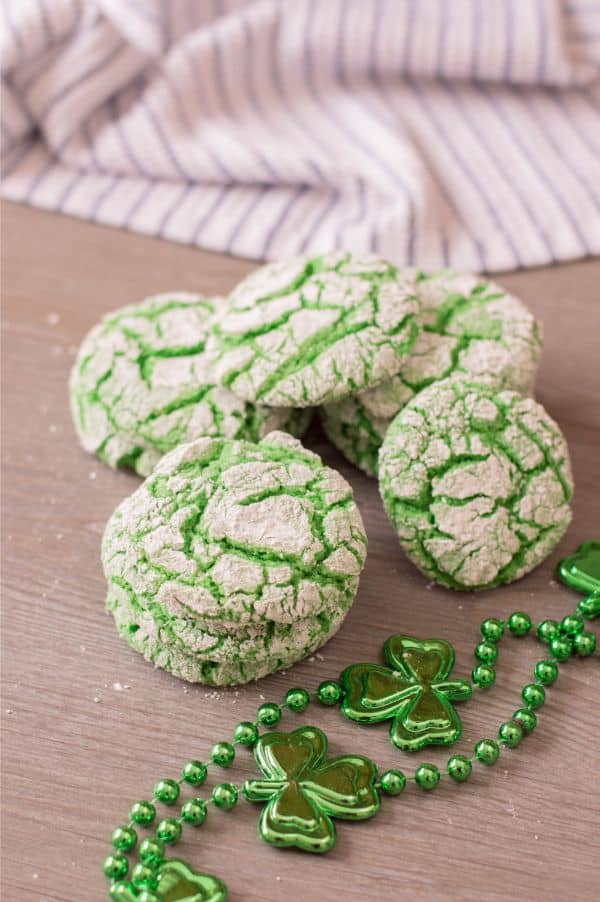 green cookies on a brown table with green beads with clovers on them and a cloth in the background
