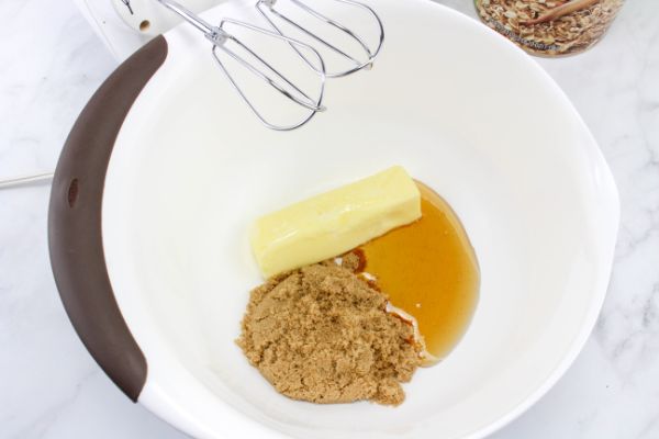 Butter, brown sugar, and honey in a white mixing bowl with beaters above it