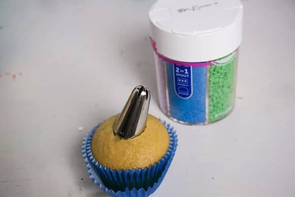 a cupcake with a piping tip in the middle next to a jar of sprinkles