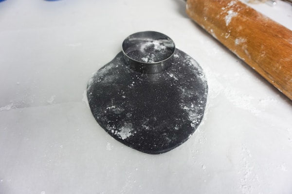 a round cookie cutter on black fondant next to a rolling pin 