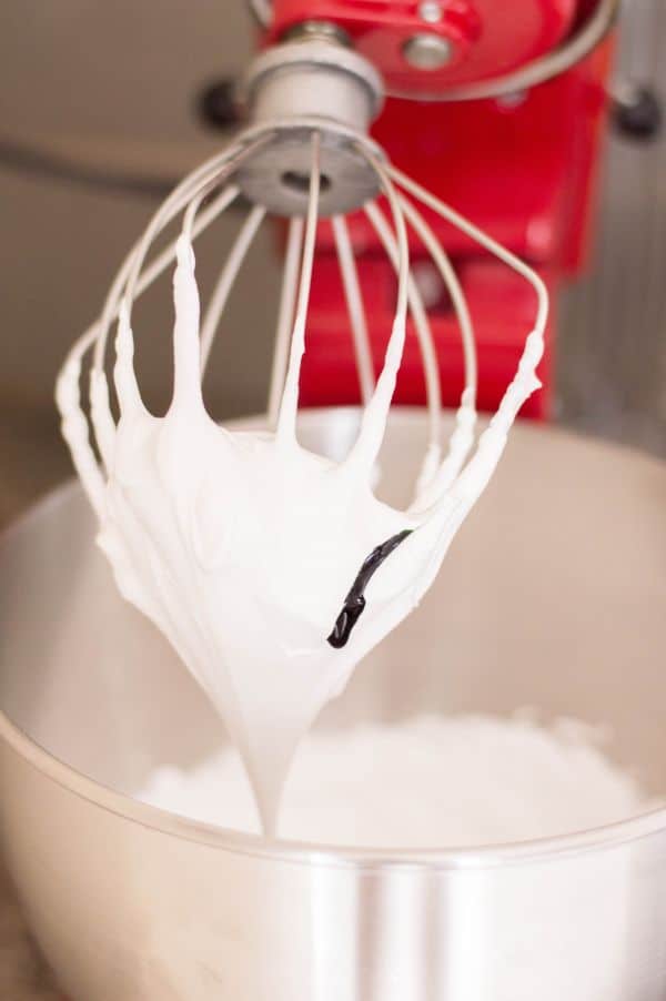 a mixer with egg white mixture on the beater above a bowl of more egg white mixture