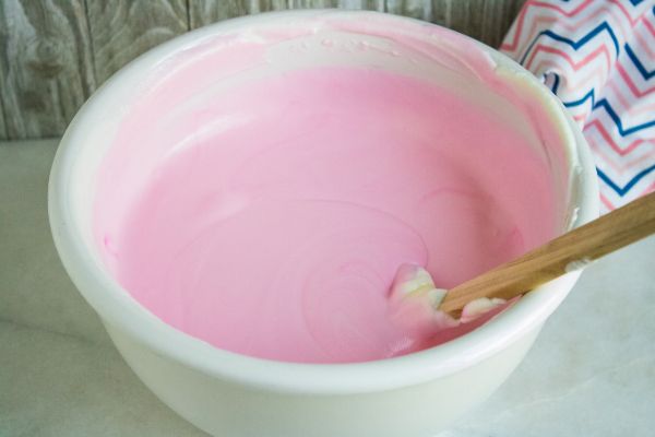 sweetened condensed milk, pink food coloring and peppermint extract in a white bowl with a spatula in it