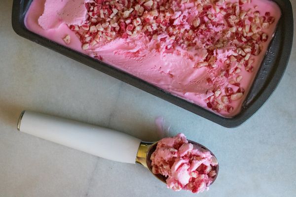 the best peppermint ice cream topped with peppermint candy in a loaf pan on a counter next to an ice cream scoop