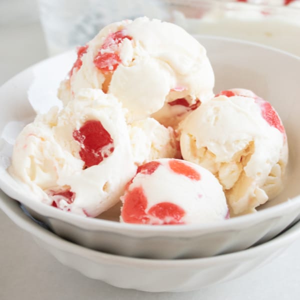 homemade candied cherry ice cream in a white bowl on a white table with more ice cream in a dish in the background