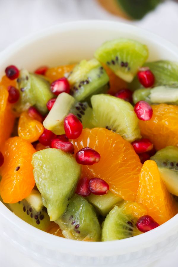 Kiwi Fruit Salad in a white bowl with halved kiwis in the background