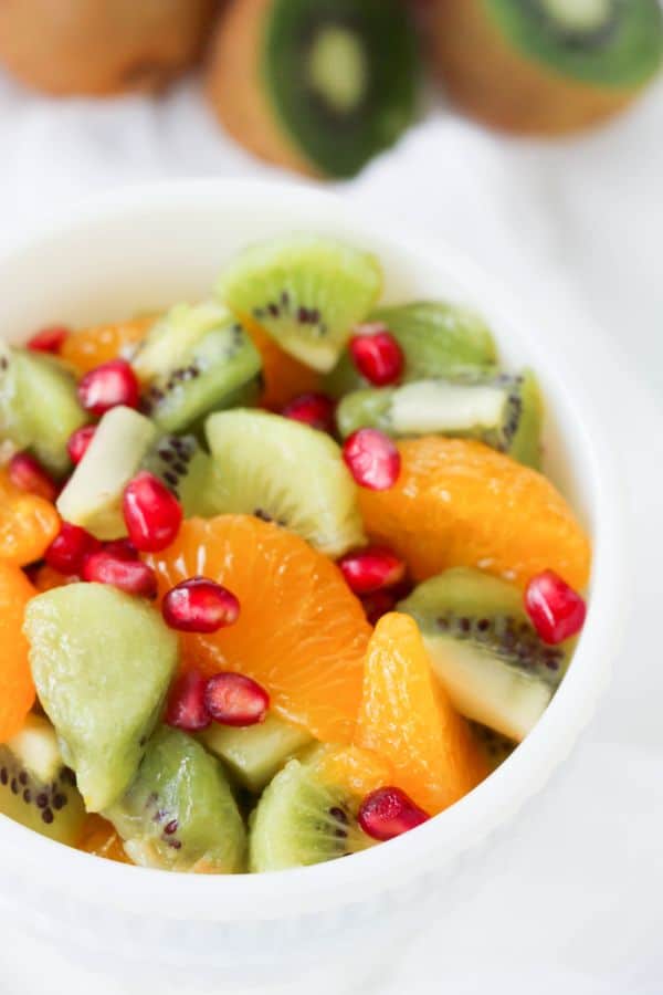 Kiwi Fruit Salad in a white bowl with halved kiwis in the background
