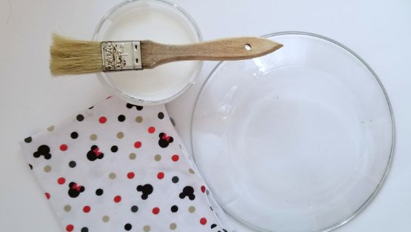 a paint brush on a mod podge can, next to a clear cake plate and Mickey mouse fabric
