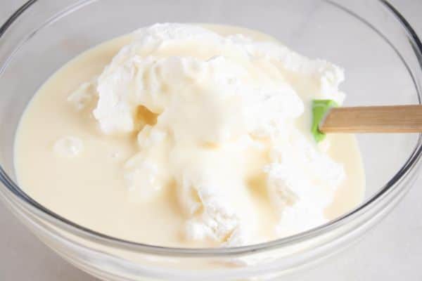 condensed milk, vanilla and cream in a glass bowl with a spatula in it