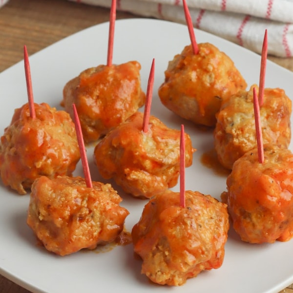 a close up of buffalo chicken meatballs with toothpicks in them on a white plate on a brown table with a red and white cloth in the background