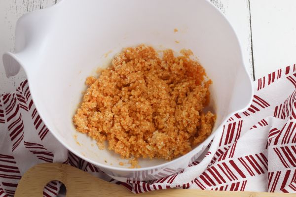 panko bread crumbs, buffalo sauce and an egg in a white mixing bowl on a red and white cloth next to a wooden spoon