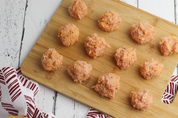 raw buffalo chicken meatballs on a wooden cutting board on a white wood table next to a red and white cloth