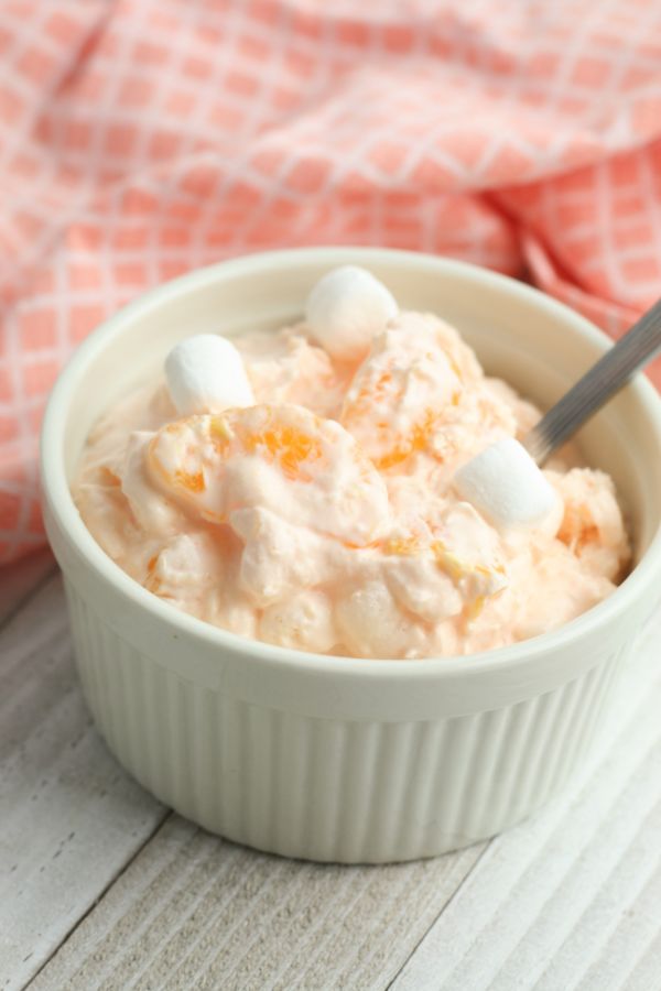 Weight Watchers Orange Fluff in a white bowl with a spoon in it on a brown table next to an orange cloth