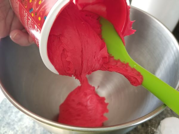 red frosting being put in a metal mixing bowl