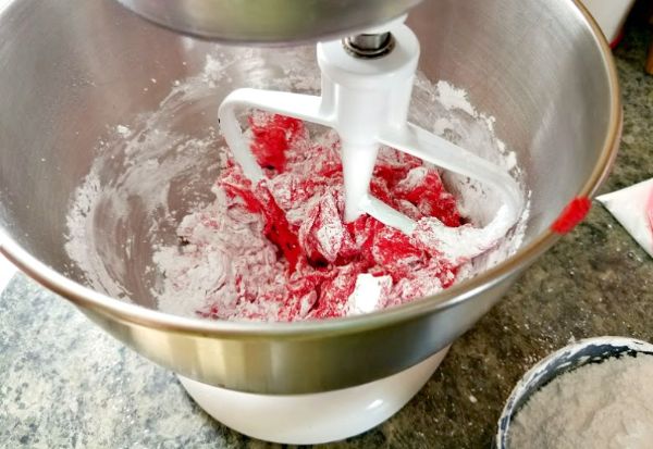 powdered sugar and red frosting being mixed in a metal mixing bowl
