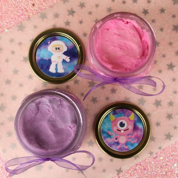 overhead view of pink and purple Edible Outer Space Play Dough on a pink star paper in two jars with alien stickers on the lids