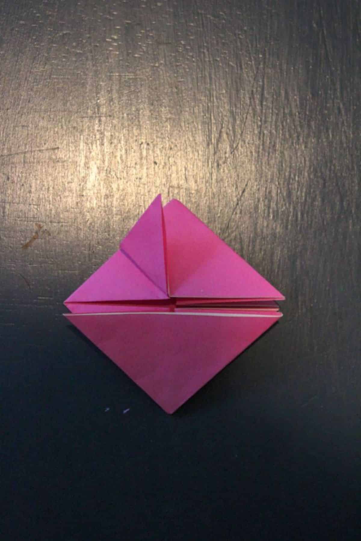 on a black background, pink origami paper top left corner is folded with the triangle up.
