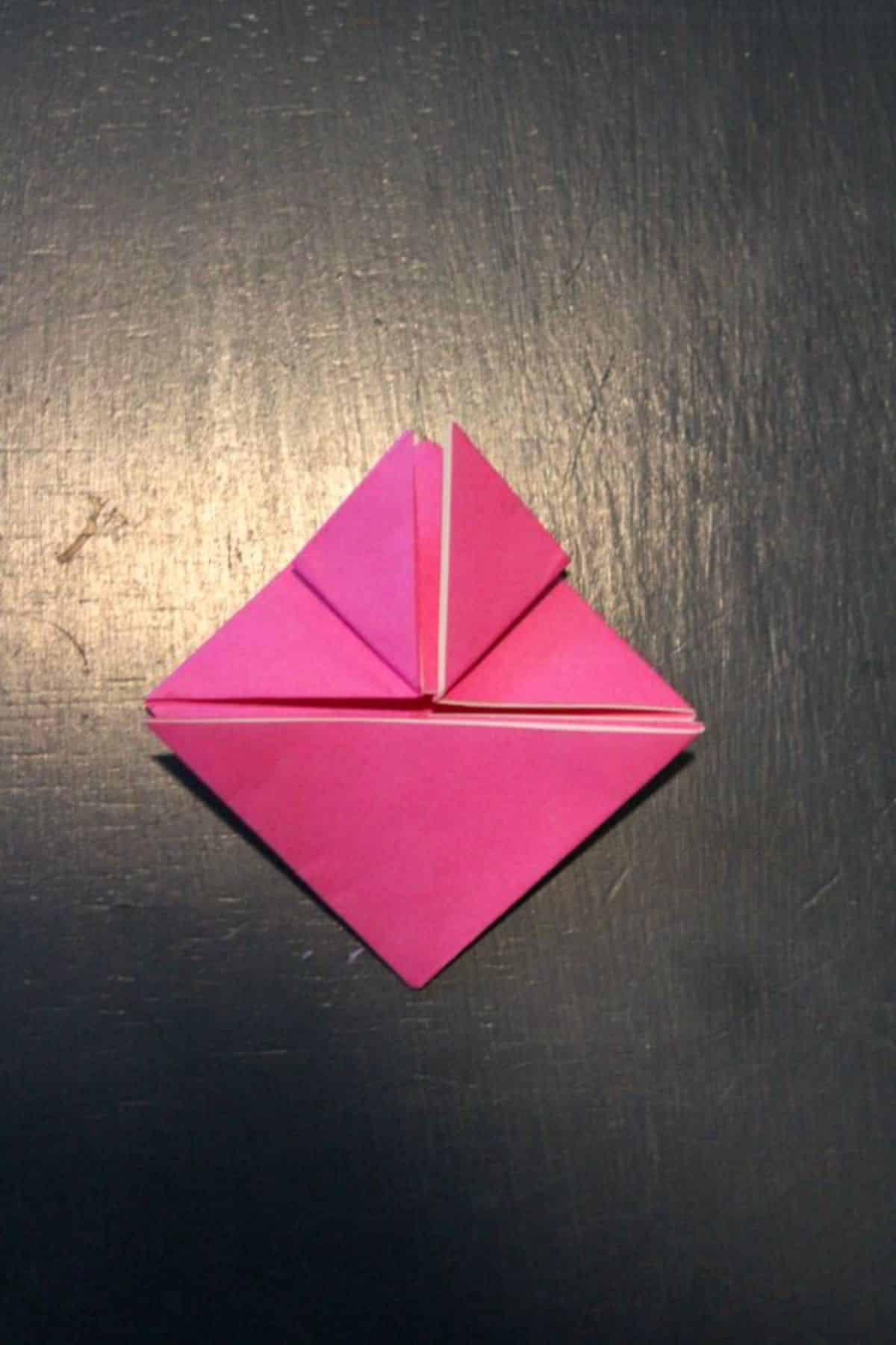 on a black background, pink origami paper top right corner is folded with the triangle up.