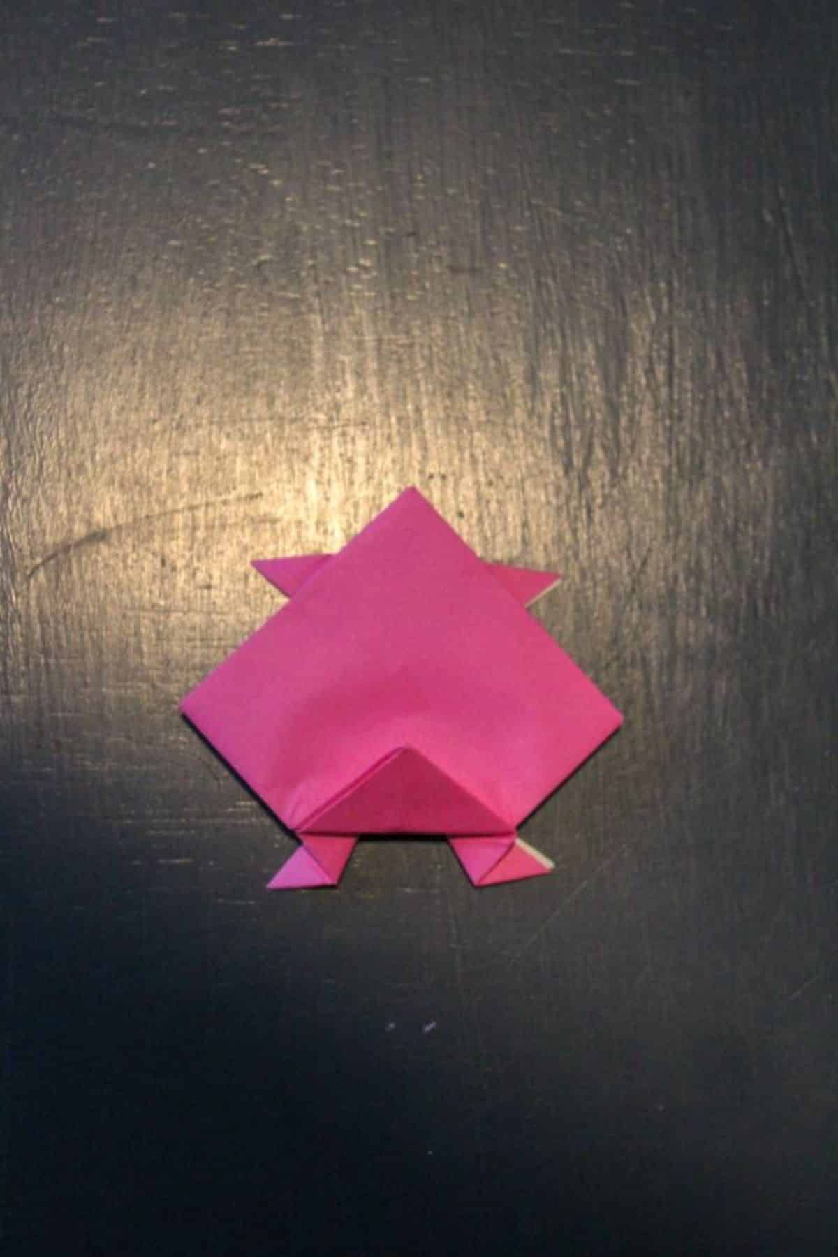 pink origami paper is folded to look like it has legs on a black background.