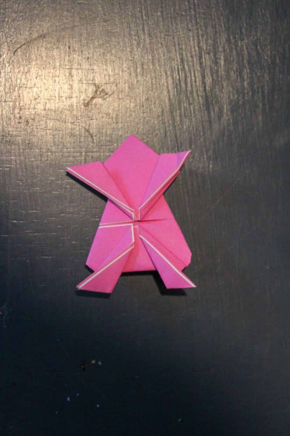 pink origami paper folded to look like a frog on a black background.