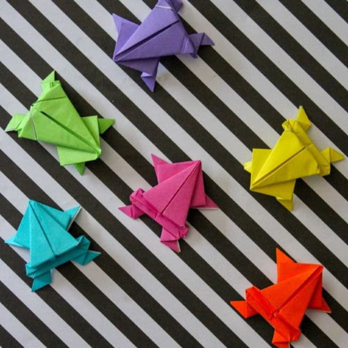 multi-colored origami frogs on a black and white striped background.