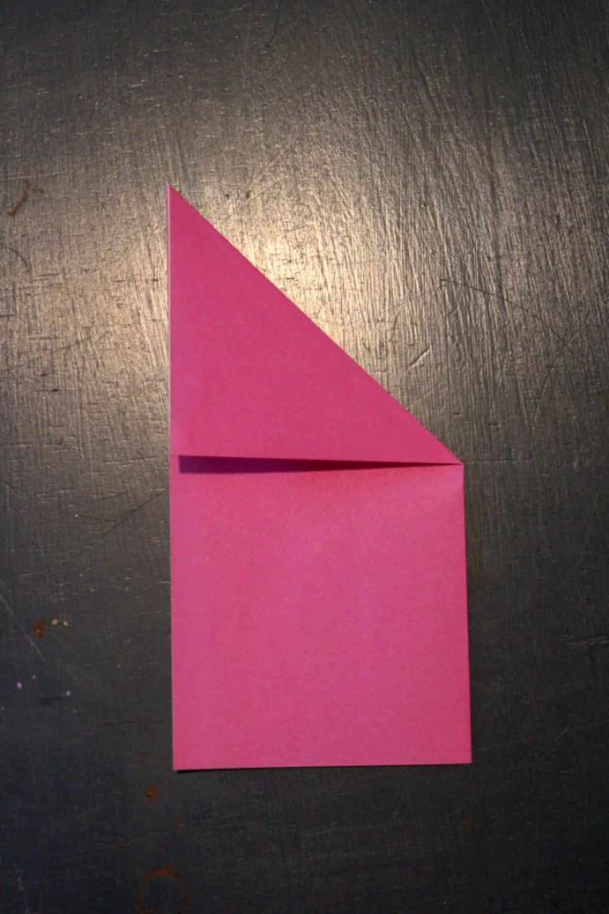 pink origami paper folded into diagonal on top right corner on a black background.