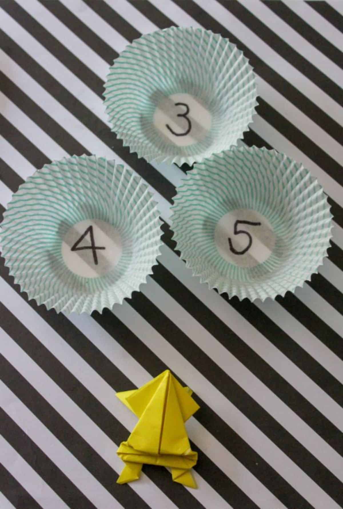 origami jumping frog and cupcake liners to jump into on a black and white striped background.