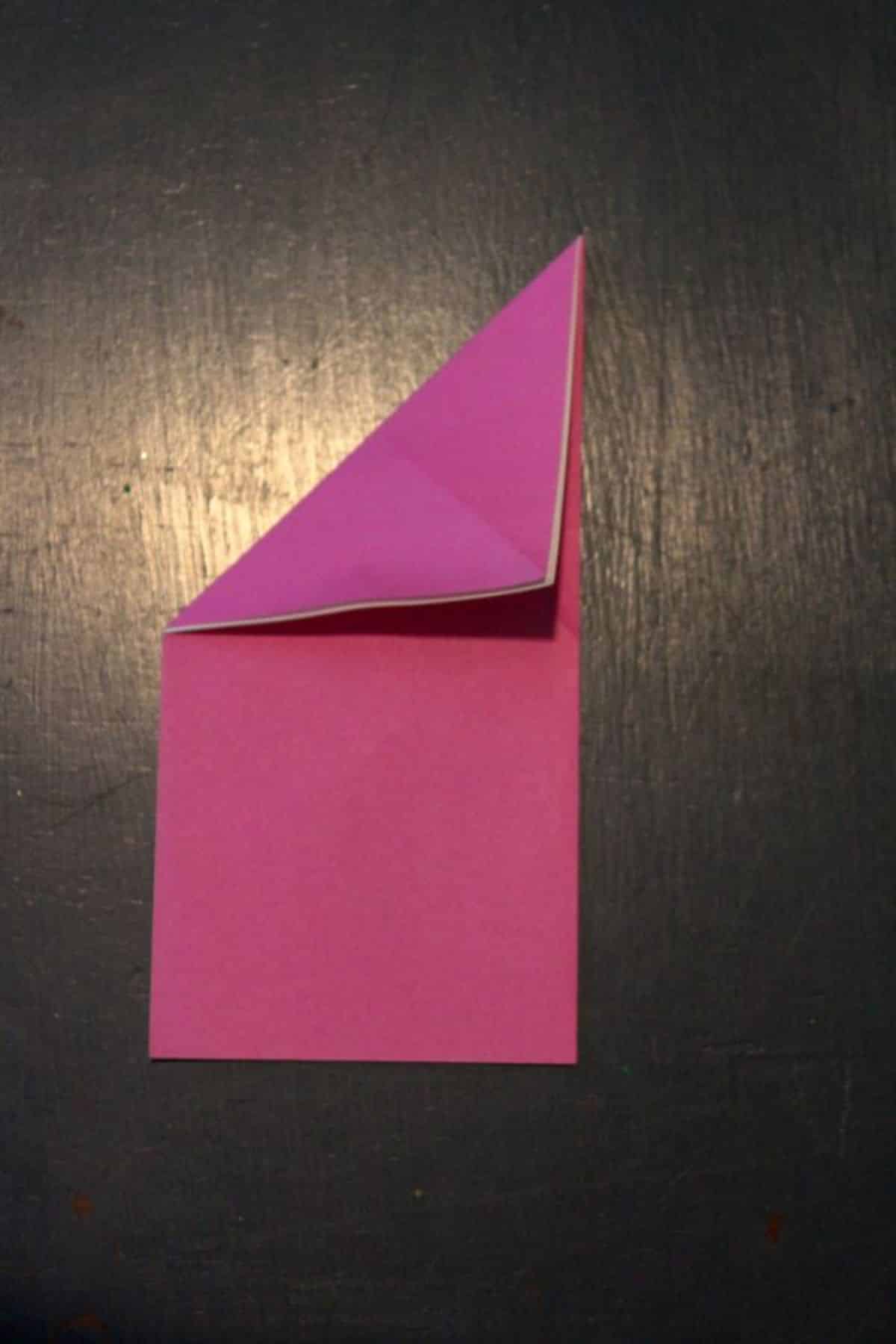 pink origami paper folded into diagonal on top left corner on a black background.