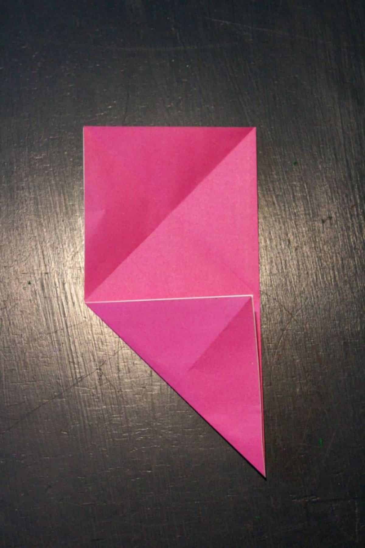 pink origami paper folded into diagonal on lower left corner on a black background.