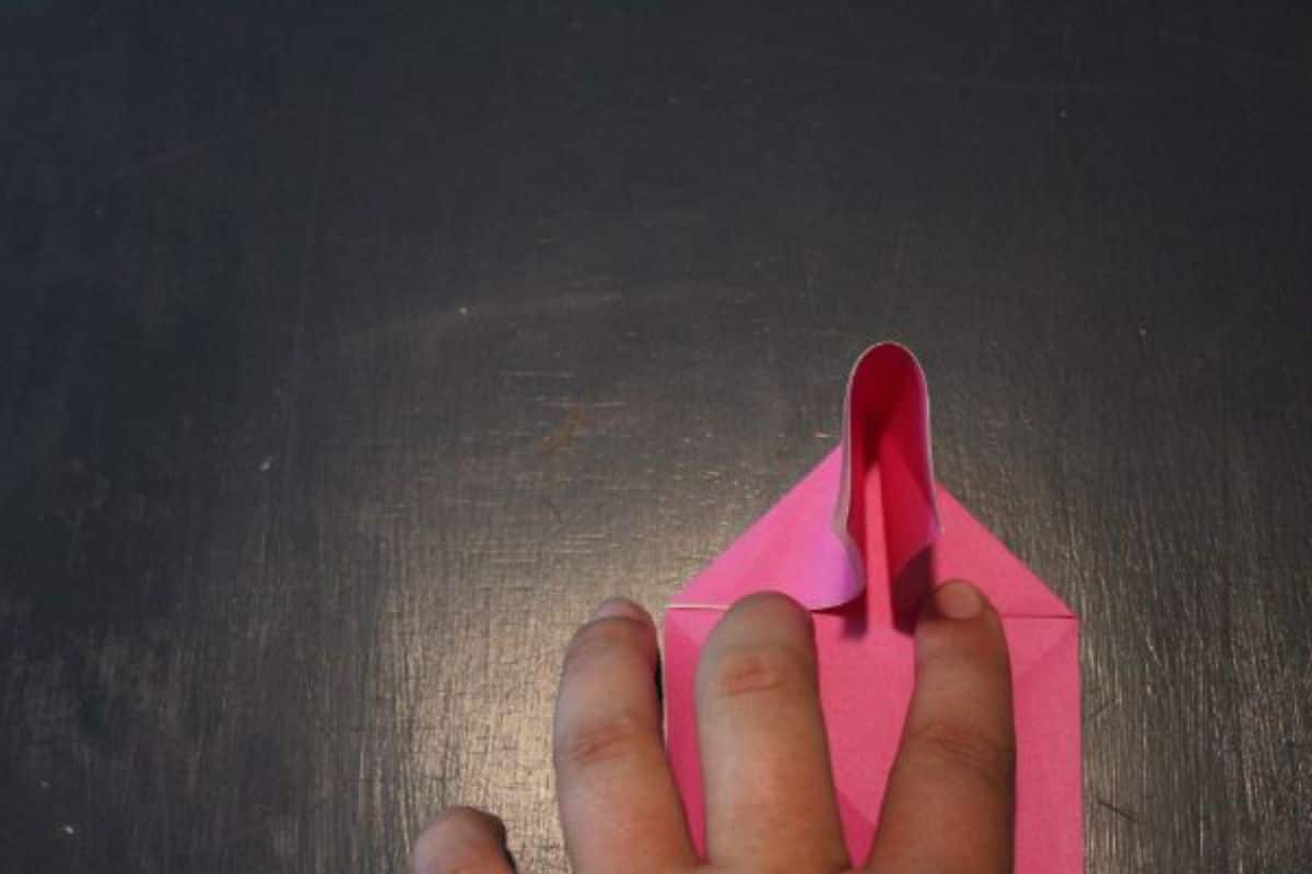 on a black background, the top half of a pink origami paper is folded using fingers.