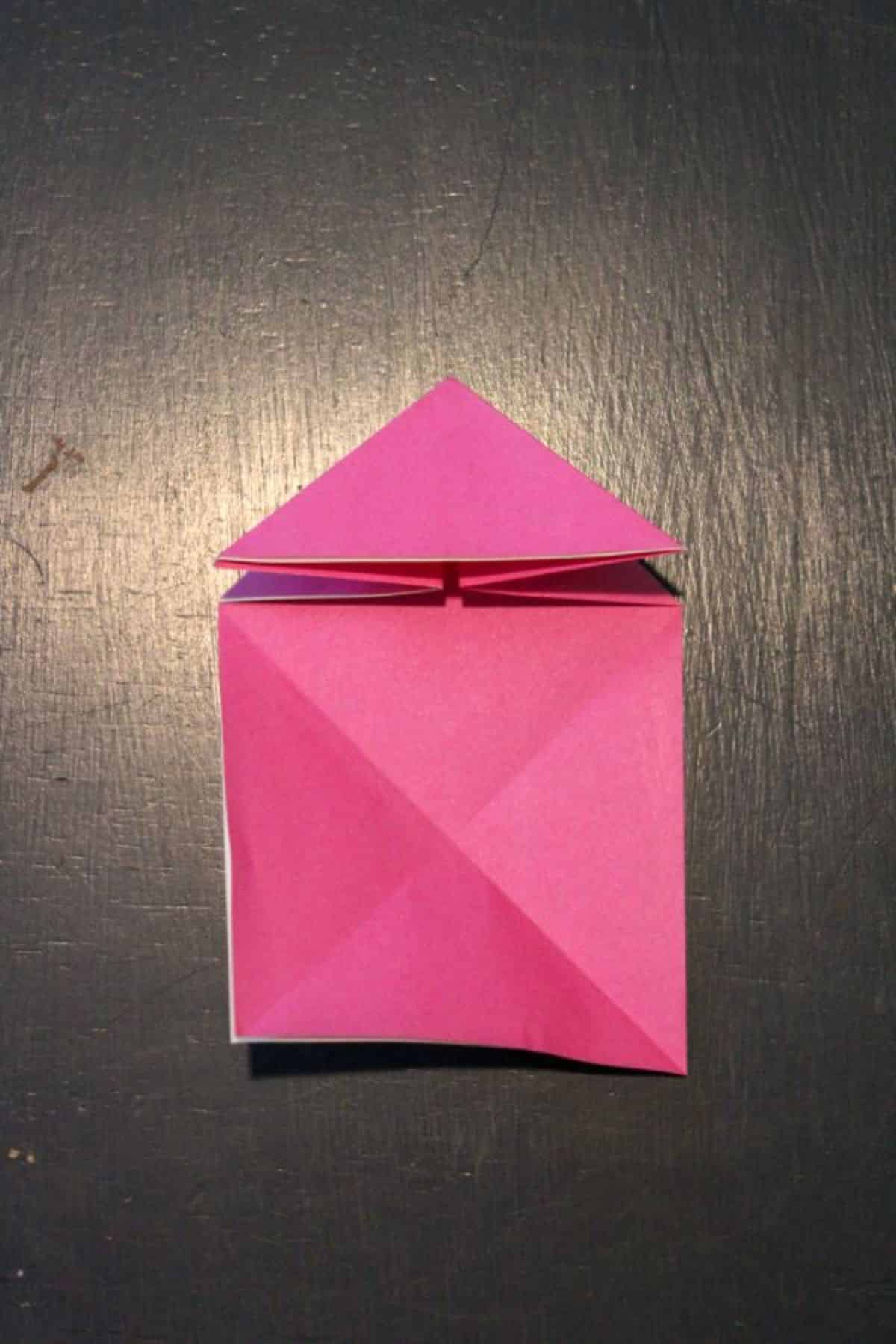 on a black background, the pink origami paper is folded like a little house.