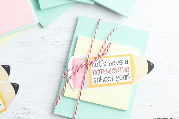 teacher notebook gift of notebook paper, a sticky note and a paper shaped like a pencil with the words Lets have a noteworthy school year on it, all tied together with red and white string