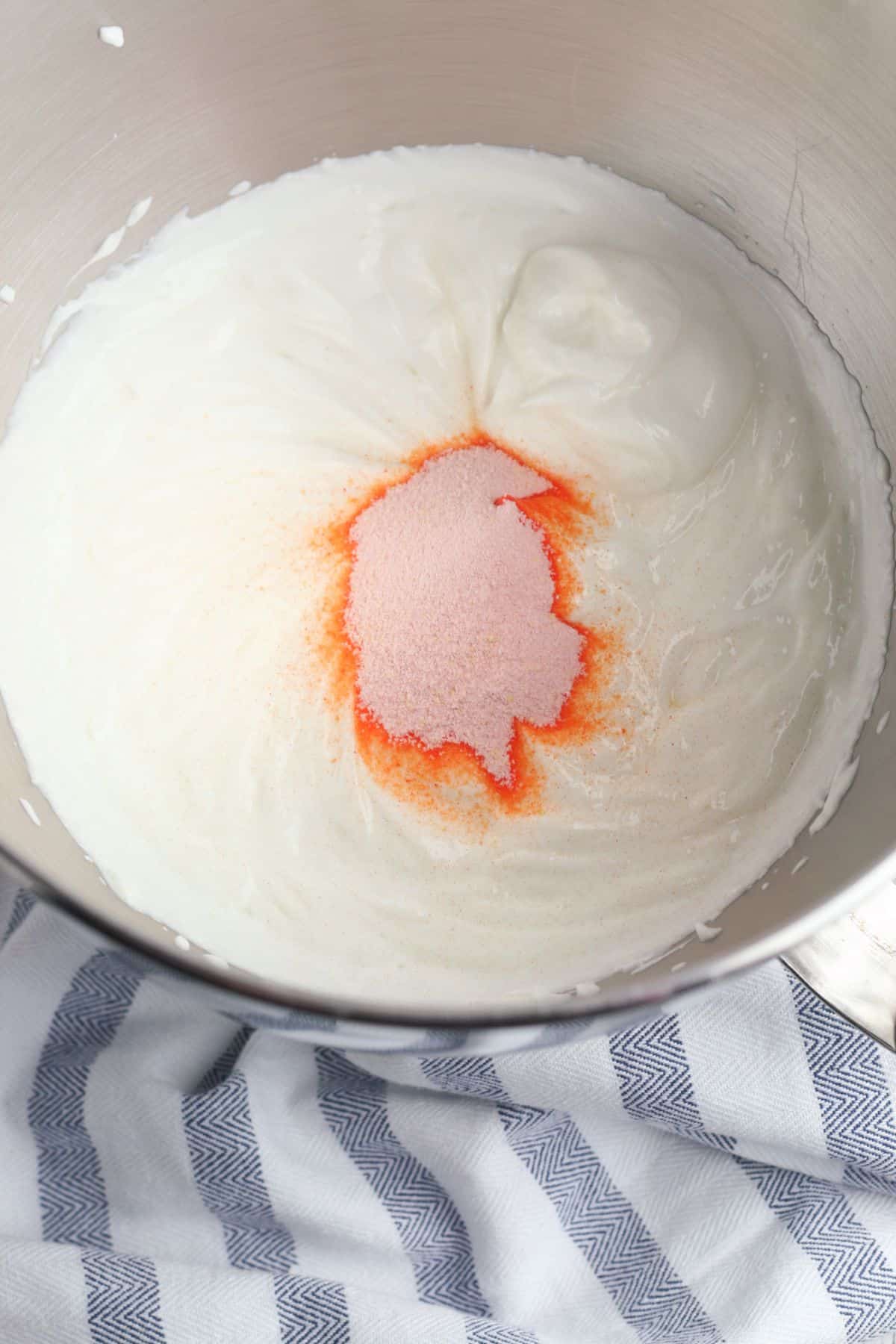 orange jello powder and Greek yogurt in a metal mixing bowl on a striped blue cloth.