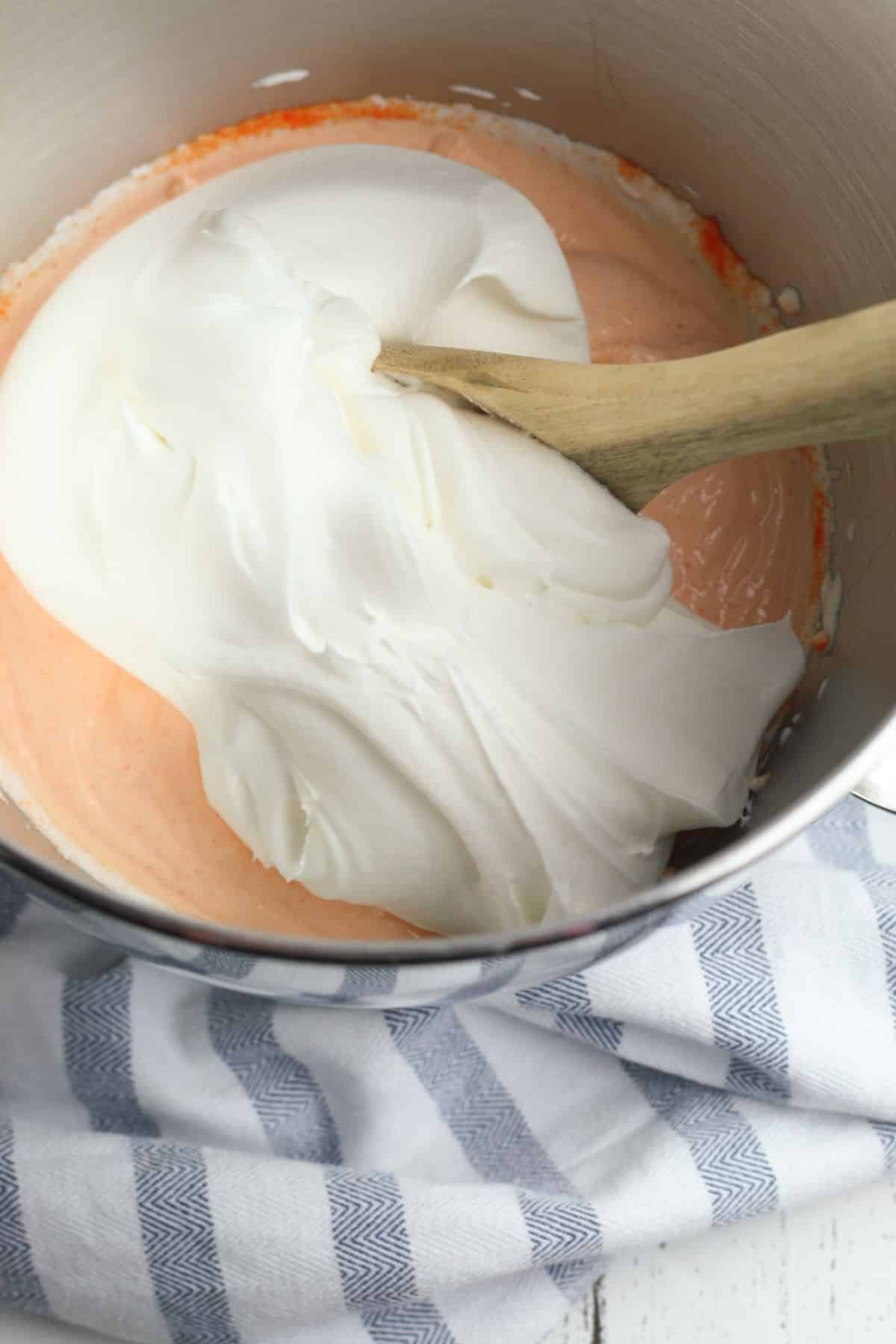 orange jello powder, whipped topping and Greek yogurt in a metal mixing bowl with a wooden spoon.