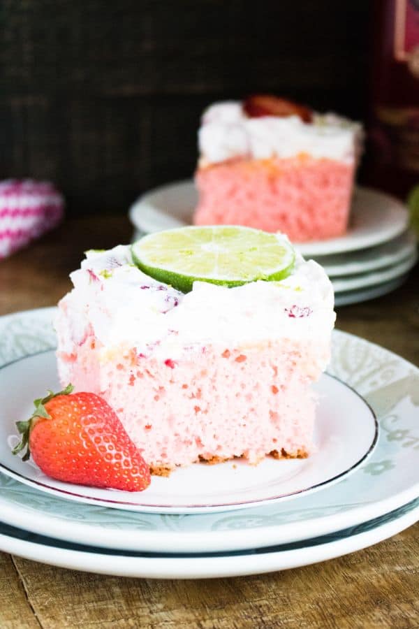 a slice of Strawberry Lime Margarita Poke Cake on top of two stacked saucers with another slice in the background