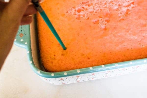 a hand using a skewer to poke holes in the strawberry margarita cake