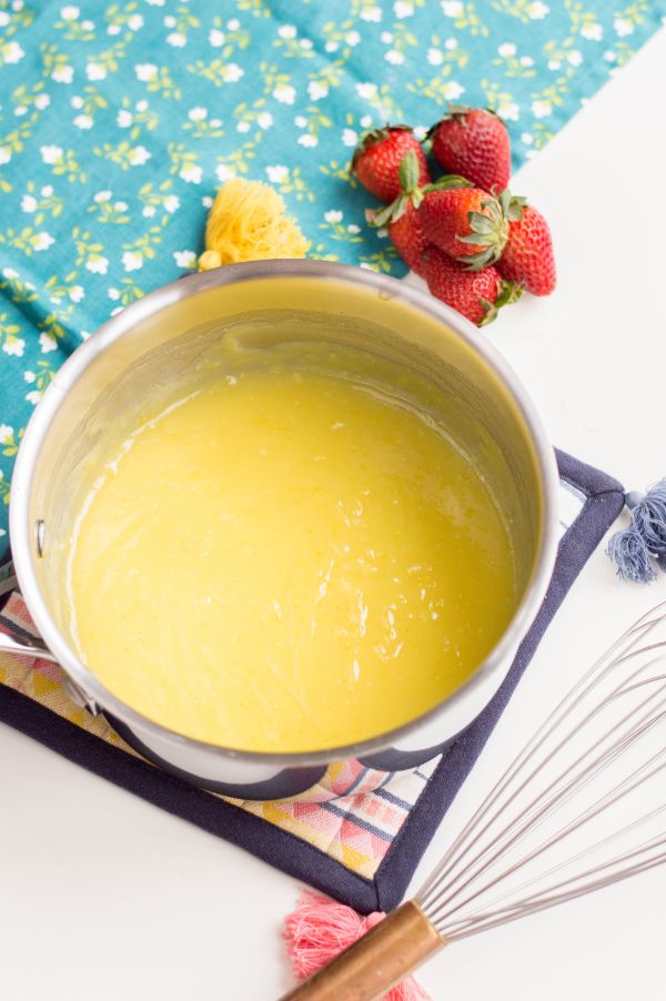 custard in a pot next to strawberries and a blue cloth with flowers on it