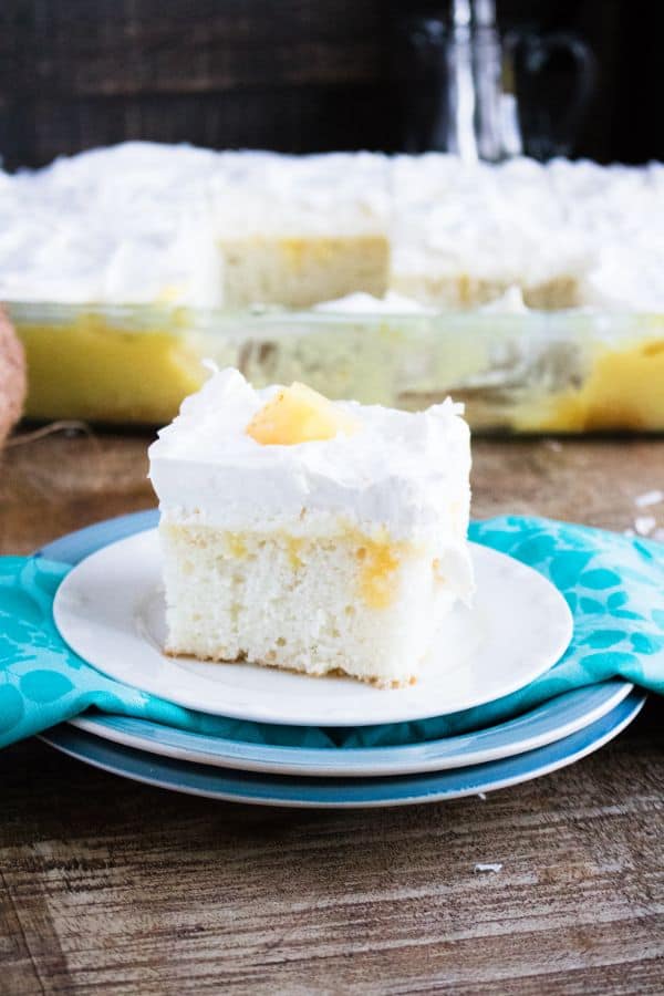 delicious slice of pina colada poke cake on plate with more cake in a glass dish in the background