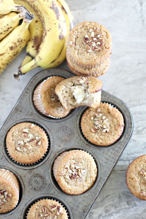 Cream Cheese Filled Banana Bread Muffins in a muffin tin and on a table next to bananas