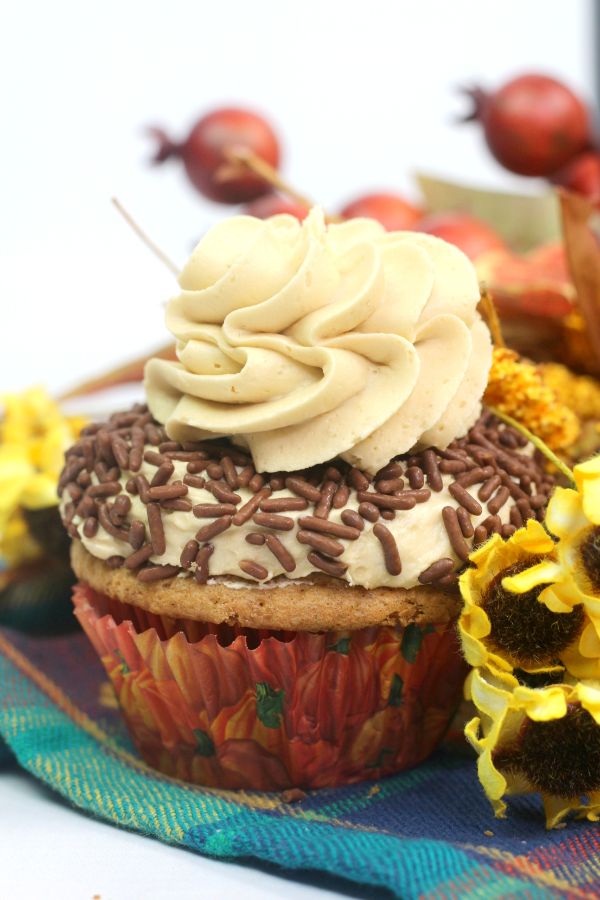 closeup of a Pumpkin Spice Cupcake with Buttercream Frosting Recipe and chocolate sprinkles on a multi-colored checkered cloth next to yellow flowers