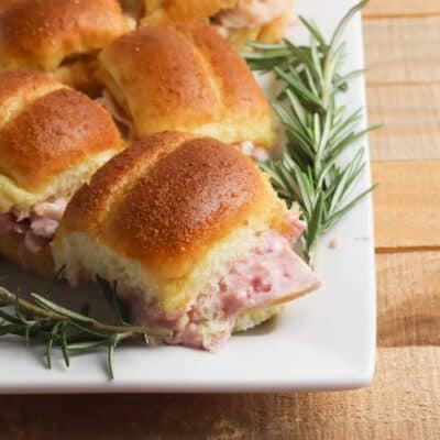 Turkey cranberry sliders with rosemary sprigs on a white plate.