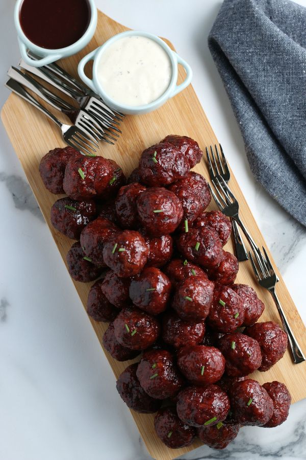 easy crockpot grape jelly BBQ meatballs next to forks and white sauce in a bowl on a wooden board