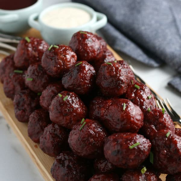 closeup of easy crockpot grape jelly BBQ meatballs next to forks and white sauce in a bowl on a wooden board
