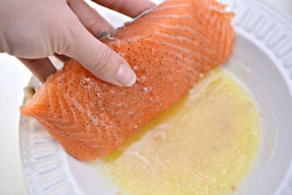 a hand dipping salmon in liquid in a white dish
