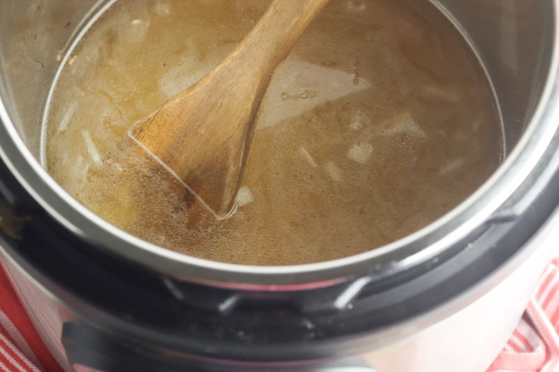 Chicken broth and sauteed onions in an instant pot with a wooden spoon.
