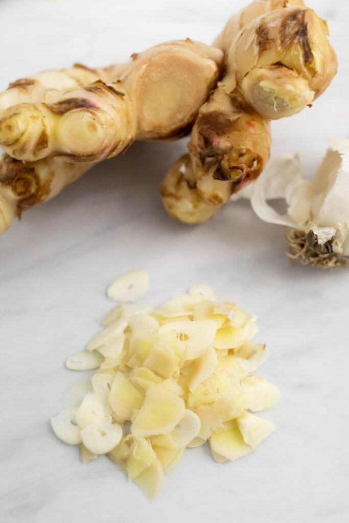 Whole Ginger and garlic and chopped ginger and garlic on a white surface.