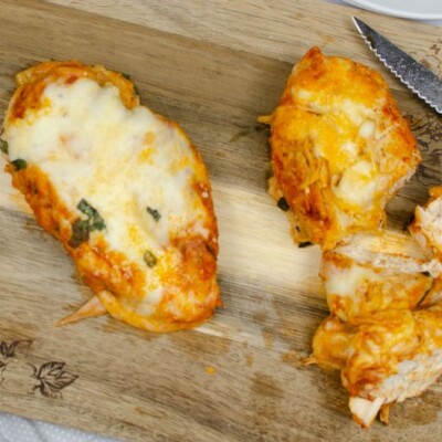 Whole chicken parmesan breast and chopped chicken parmesan on a wooden chopping board.