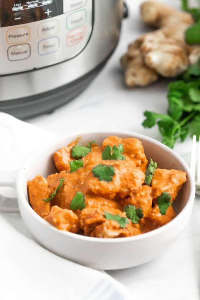 Chicken tikka masala in a white bowl next to ginger and an instant pot.