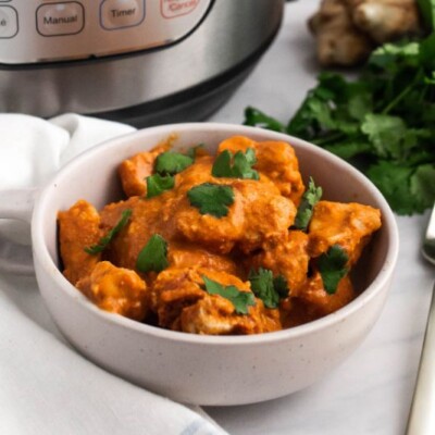Chicken tikka masala in a white bowl next to a fork, cilantro, ginger and an instant pot.