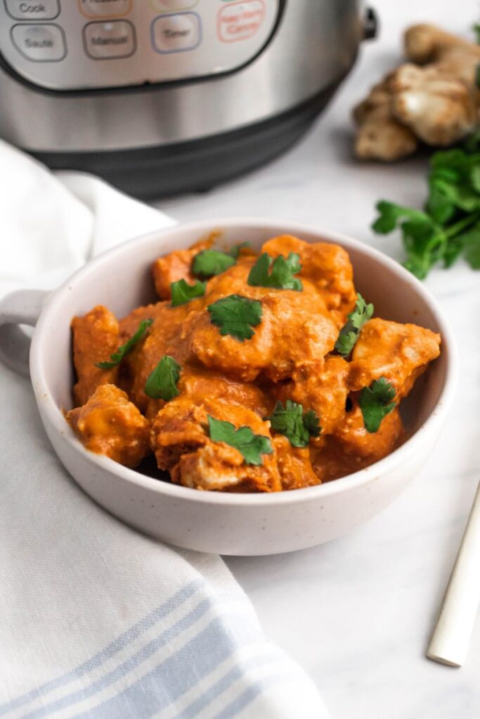 Chicken tikka with cilantro in a white bowl next to an instant pot.